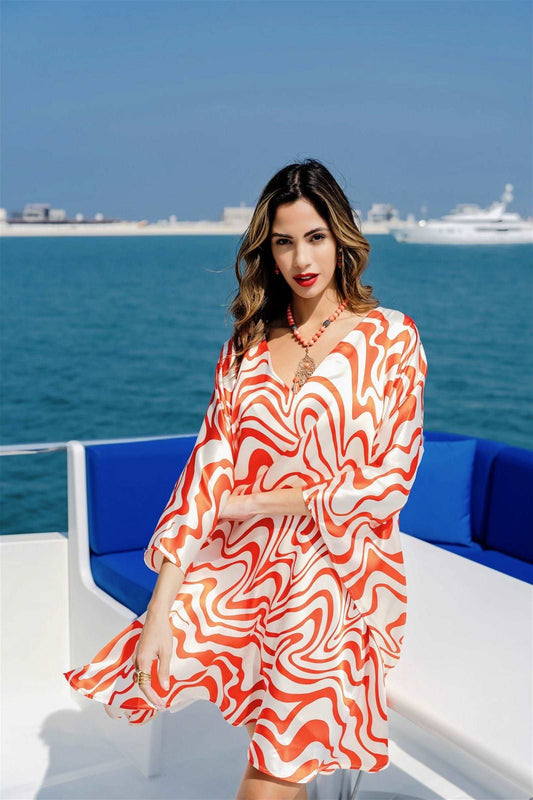 The model in the image is wearing Printed Orange Colour Kaftan In Silk Fabric from Alice Milan. Crafted with the finest materials and impeccable attention to detail, the Kaftan / Dress looks premium, trendy, luxurious and offers unparalleled comfort. It’s a perfect clothing option for loungewear, resort wear, party wear or for an airport look. The woman in the image looks happy, and confident with her style statement putting a happy smile on her face.