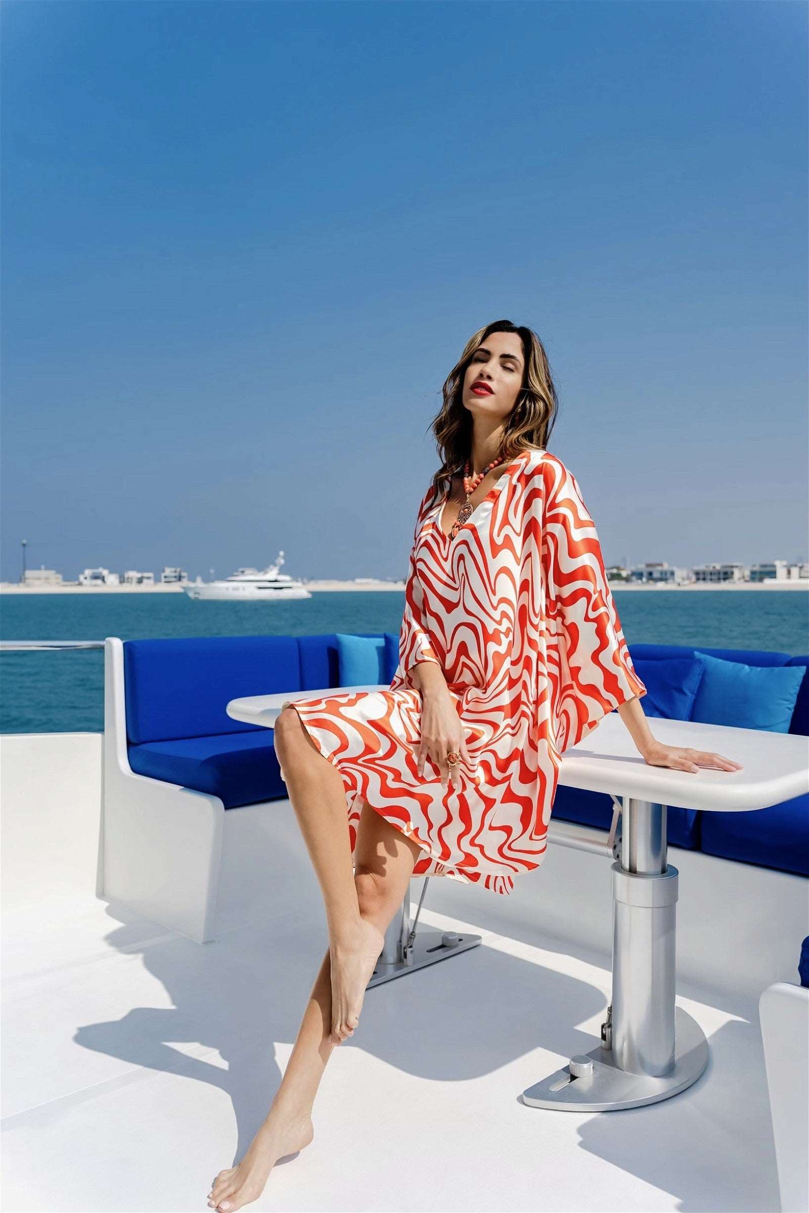 The model in the image is wearing Printed Orange Colour Kaftan In Silk Fabric from Alice Milan. Crafted with the finest materials and impeccable attention to detail, the Kaftan / Dress looks premium, trendy, luxurious and offers unparalleled comfort. It’s a perfect clothing option for loungewear, resort wear, party wear or for an airport look. The woman in the image looks happy, and confident with her style statement putting a happy smile on her face.