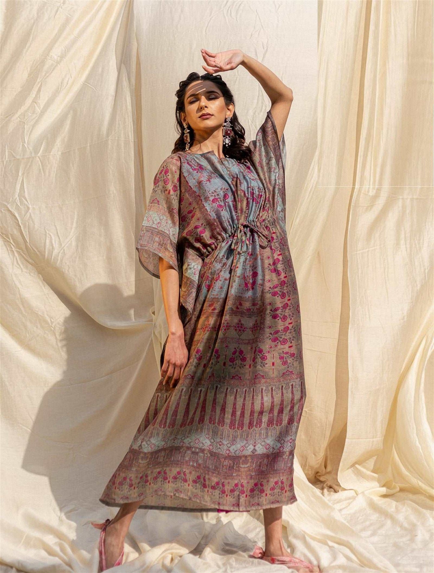 The model in the image is wearing Grey Silk Premium Kaftan from Alice Milan. Crafted with the finest materials and impeccable attention to detail, the Kaftan / Dress looks premium, trendy, luxurious and offers unparalleled comfort. It’s a perfect clothing option for loungewear, resort wear, party wear or for an airport look. The woman in the image looks happy, and confident with her style statement putting a happy smile on her face.