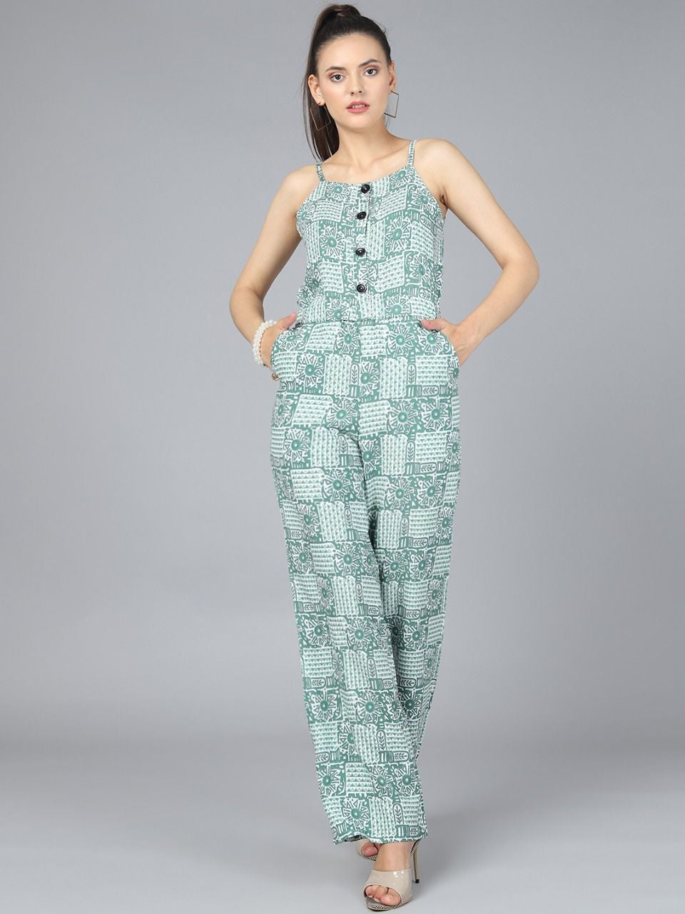 The model in the image is wearing Stylish Printed Women Jumpsuit - Teal from Alice Milan. Crafted with the finest materials and impeccable attention to detail, the Jumpsuit looks premium, trendy, luxurious and offers unparalleled comfort. It’s a perfect clothing option for loungewear, resort wear, party wear or for an airport look. The woman in the image looks happy, and confident with her style statement putting a happy smile on her face.