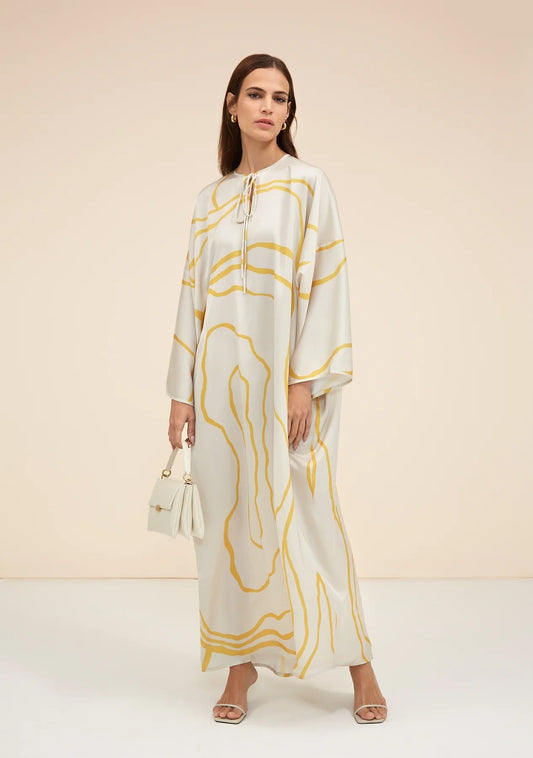 The model in the image is wearing Yellow Colour Printed Organza Silk Party Wear Kaftan from Alice Milan. Crafted with the finest materials and impeccable attention to detail, the Kaftan / Dress looks premium, trendy, luxurious and offers unparalleled comfort. It’s a perfect clothing option for loungewear, resort wear, party wear or for an airport look. The woman in the image looks happy, and confident with her style statement putting a happy smile on her face.