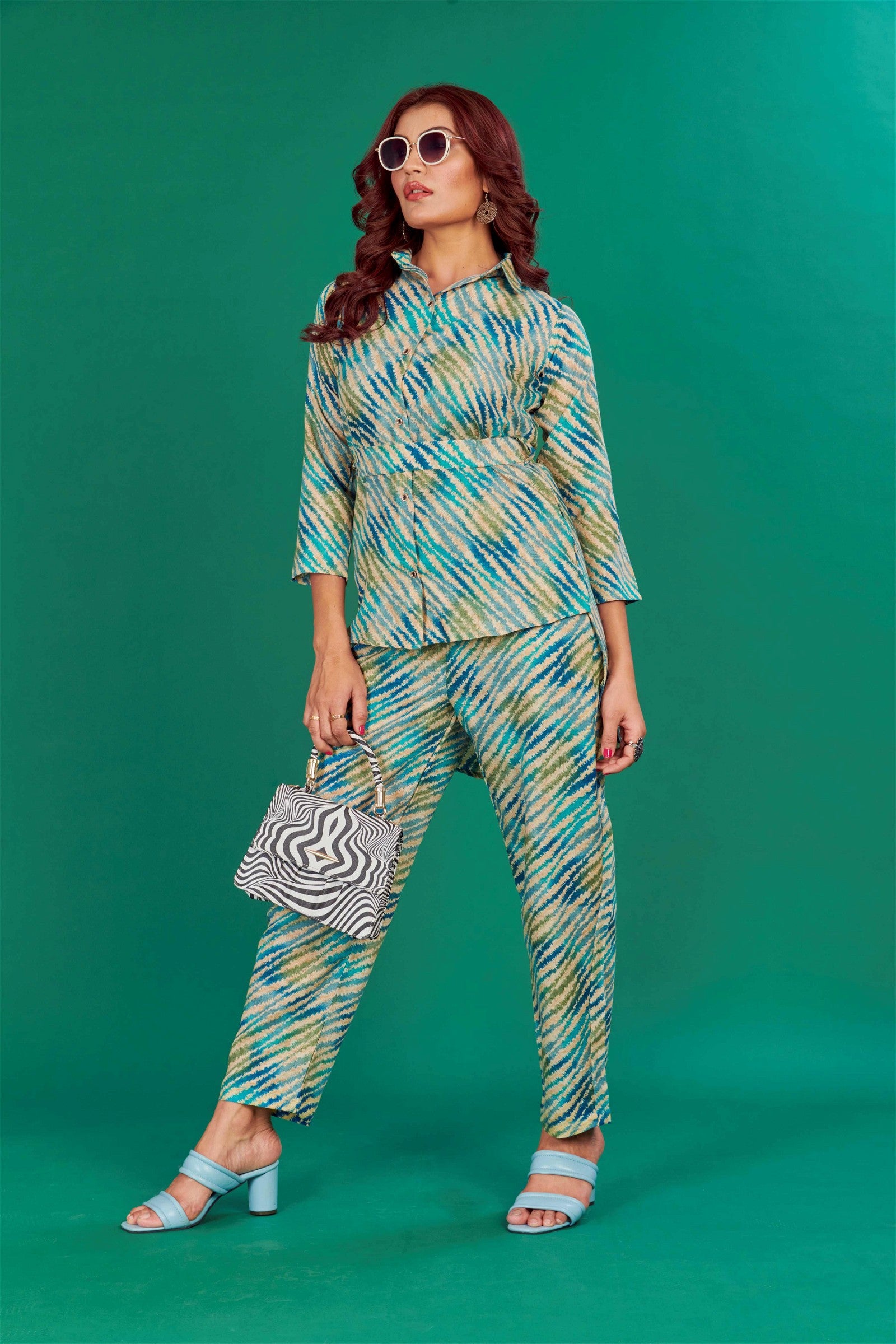 The model in the image is wearing Teal Cotton Party Wear Co-ords Set from Alice Milan. Crafted with the finest materials and impeccable attention to detail, the  looks premium, trendy, luxurious and offers unparalleled comfort. It’s a perfect clothing option for loungewear, resort wear, party wear or for an airport look. The woman in the image looks happy, and confident with her style statement putting a happy smile on her face.
