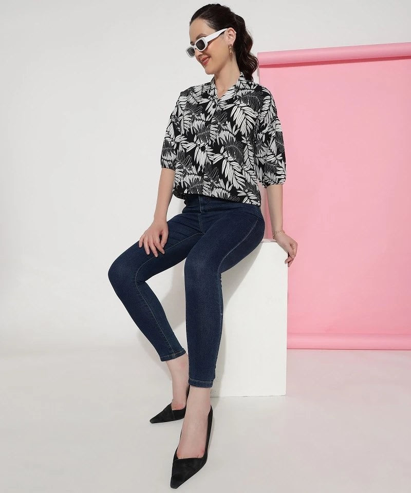 The model in the image is wearing Black Colour Casual Wear Crepe Printed Shirt For Women from Alice Milan. Crafted with the finest materials and impeccable attention to detail, the Western Wear Top looks premium, trendy, luxurious and offers unparalleled comfort. It’s a perfect clothing option for loungewear, resort wear, party wear or for an airport look. The woman in the image looks happy, and confident with her style statement putting a happy smile on her face.