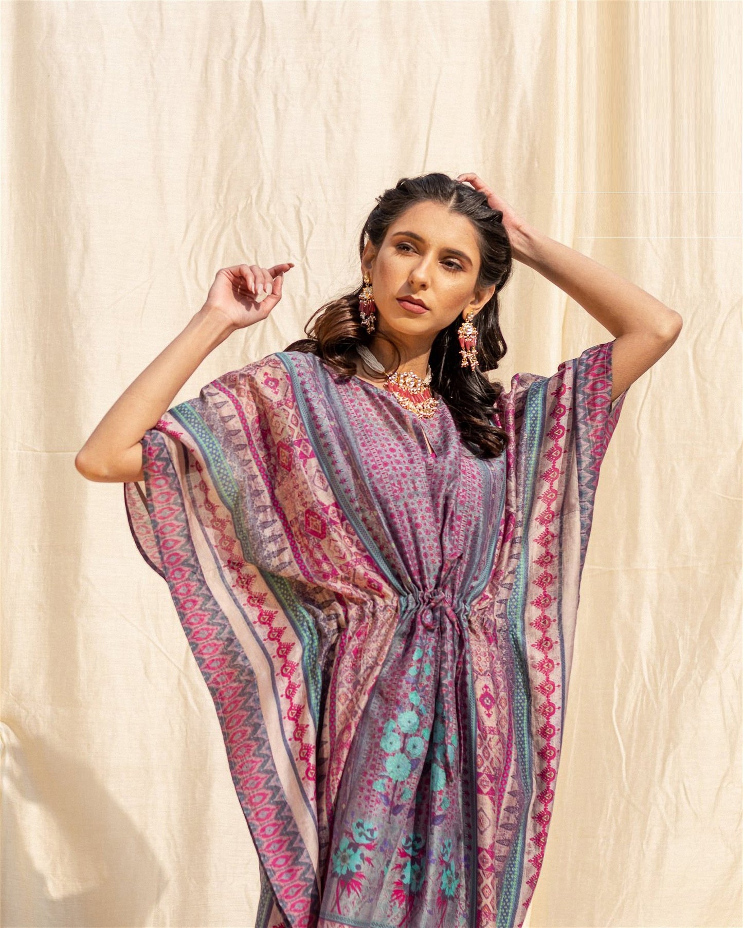 The model in the image is wearing Purple Soft Silk Premium Kaftan from Alice Milan. Crafted with the finest materials and impeccable attention to detail, the Kaftan / Dress looks premium, trendy, luxurious and offers unparalleled comfort. It’s a perfect clothing option for loungewear, resort wear, party wear or for an airport look. The woman in the image looks happy, and confident with her style statement putting a happy smile on her face.